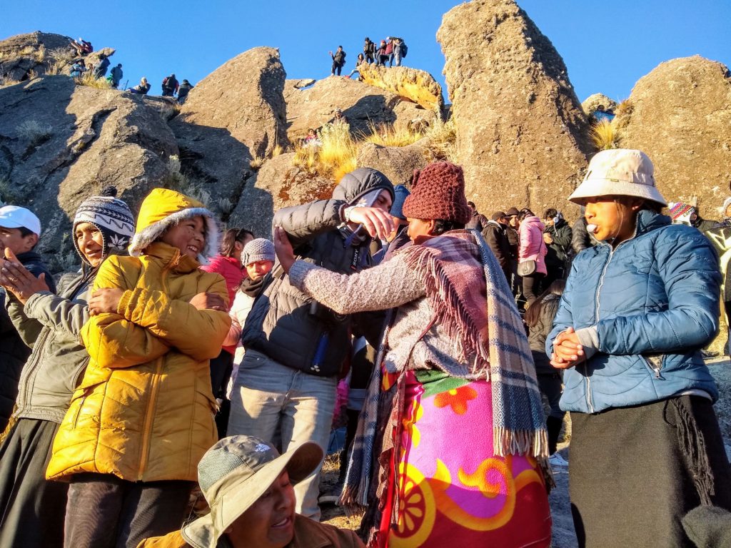 People in warm clothing hugging themselves and each other among rocky outcroppings.