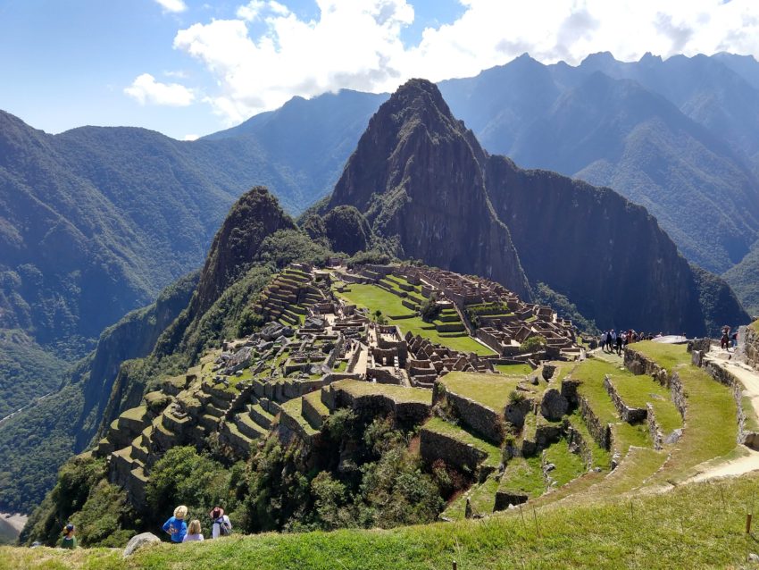 View of the Machu Picchu ruins from a viewpoint above, with tall mountains in the background.