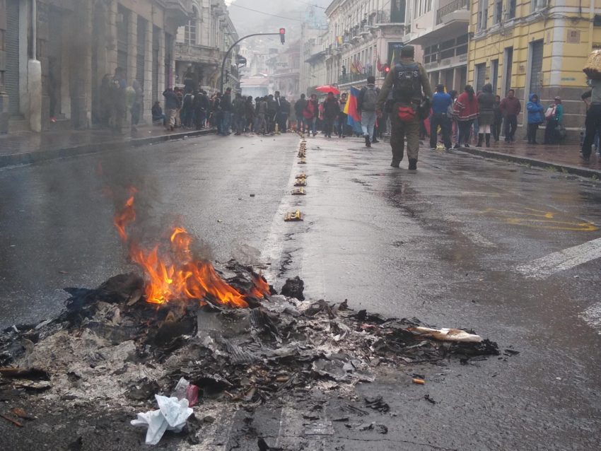Small fire in foreground; protesters in background on the streets of Quito, Ecuador