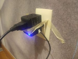 A black power adapter plugged into the wall and being held in place by masking tape.