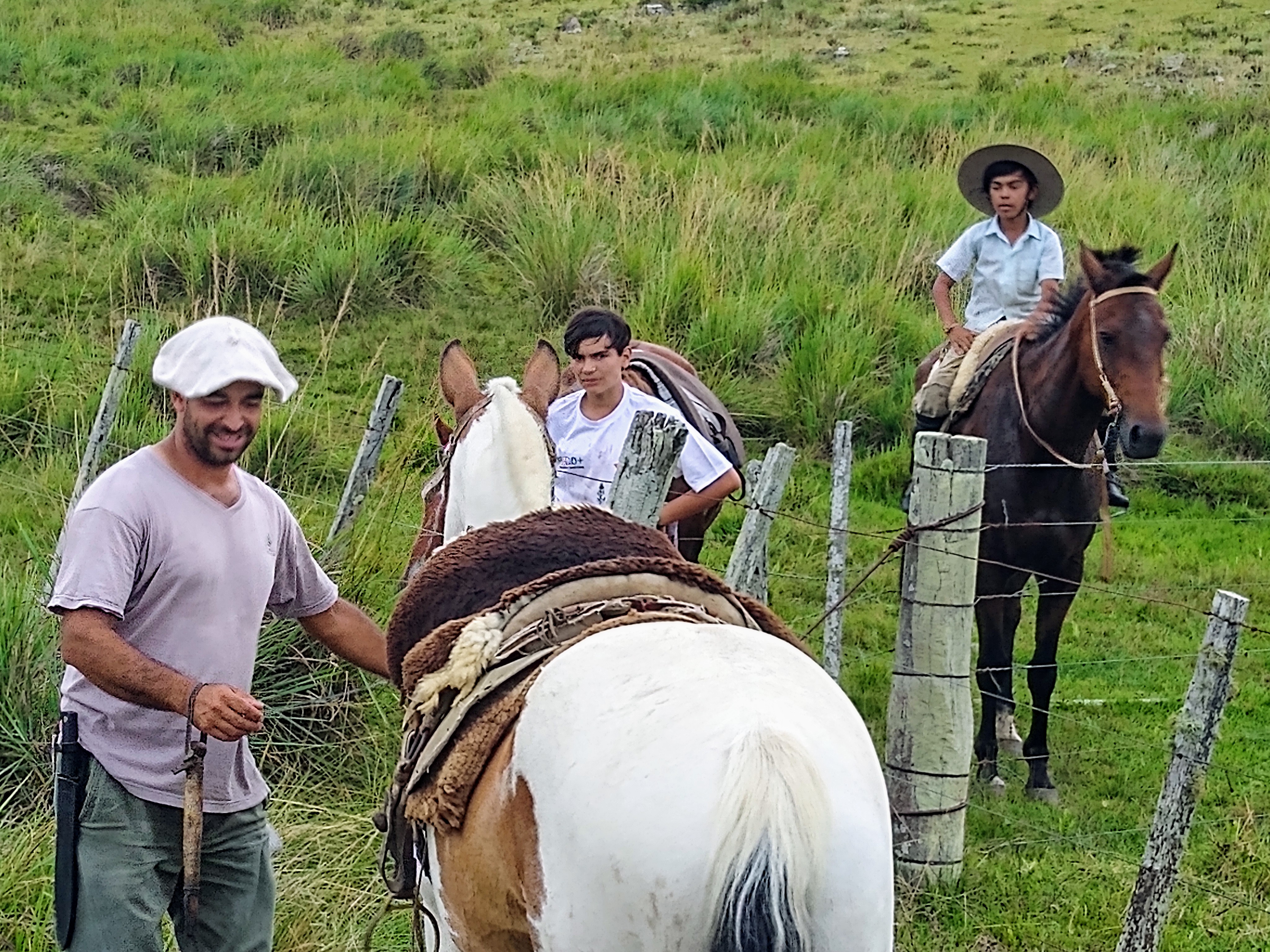 A man standing next to a horse near two young men, one on horseback and one standing on the ground by a fence.
