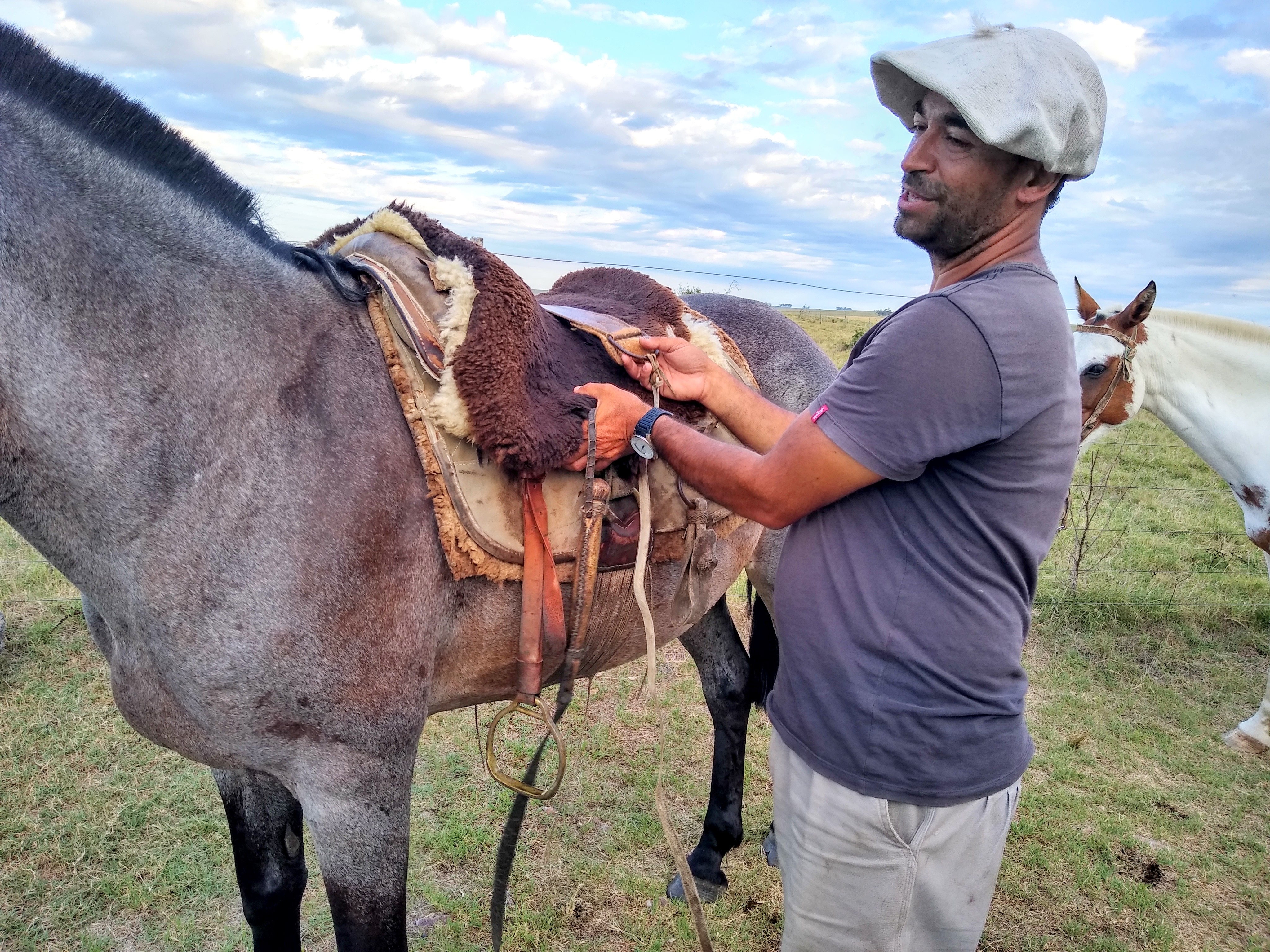 A man standing next to a horse, with his hands on the horse's saddle.