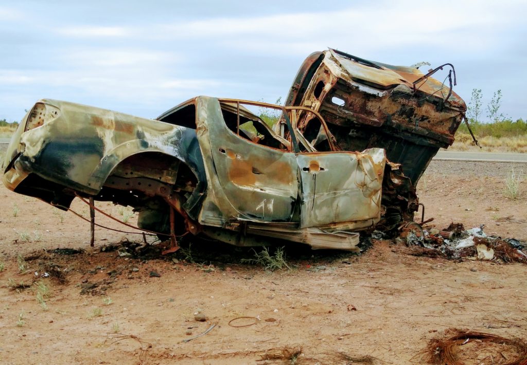 Two crashed and rusted out vehicles on the side of the highway.