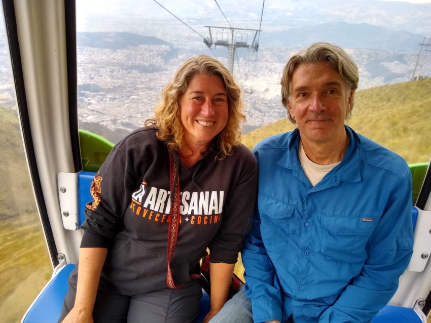 A woman and man sitting next to each other inside a cable car, smiling and looking directly into the camera.