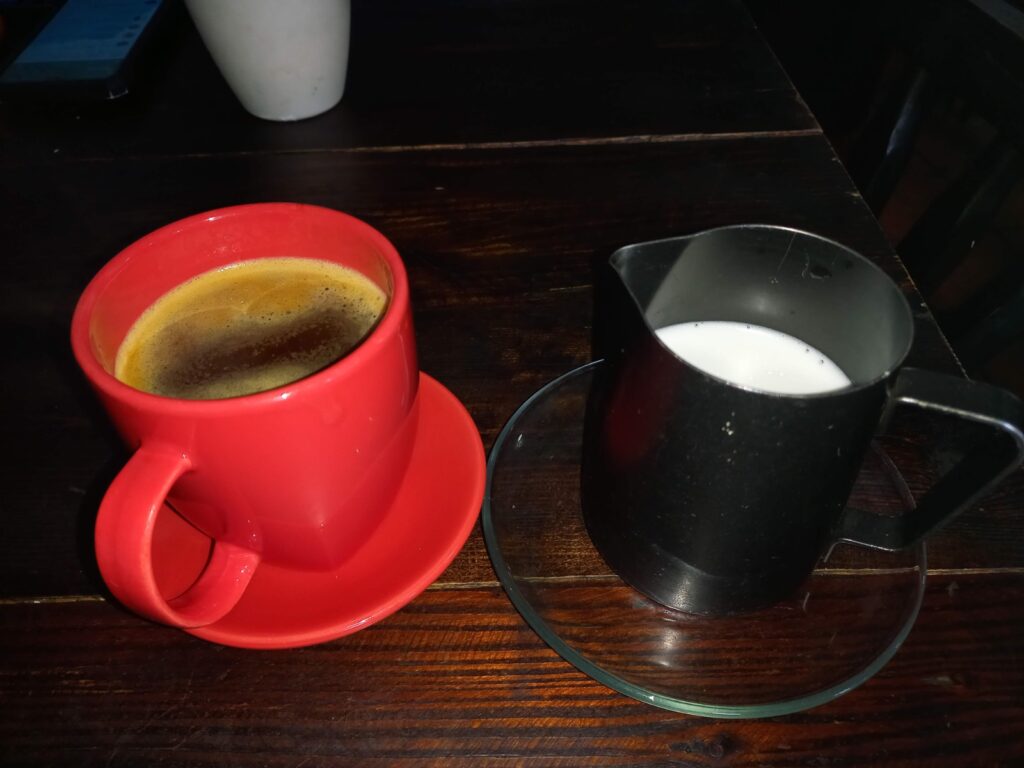a red cup filled with black coffee next to a silver cup filled with milk