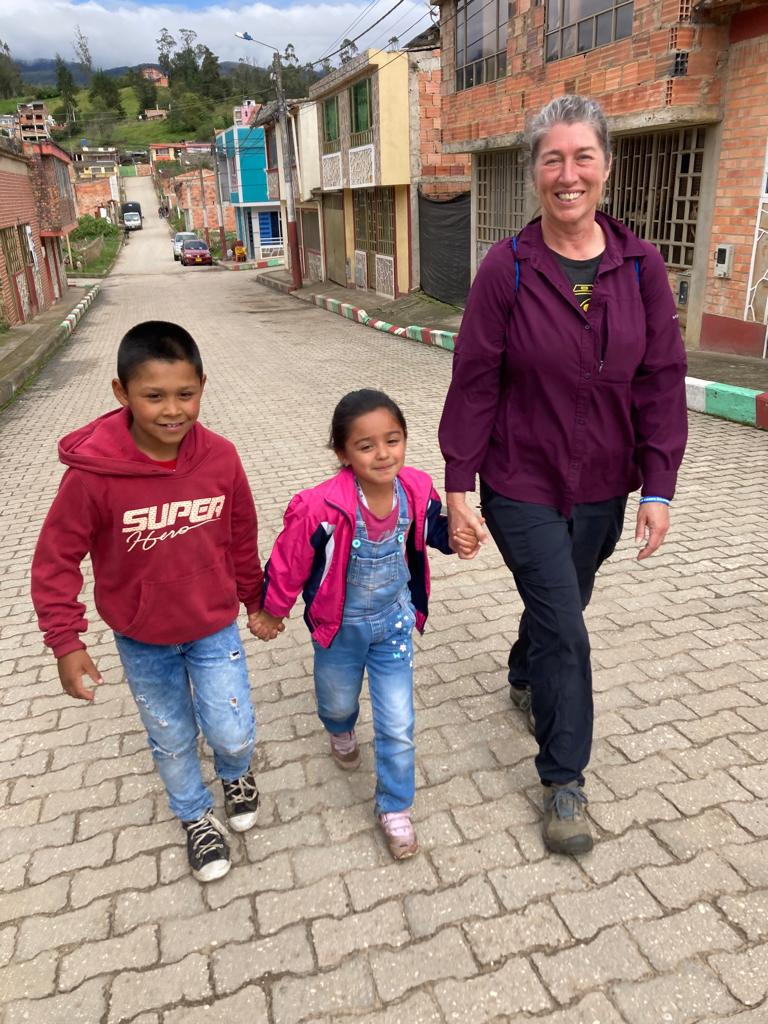A boy, a girl, and a woman walk on a brick-paved street, holding hands.
